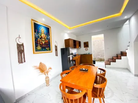 Cozy Balinese villa dining area with wooden table and chairs, kitchenette, framed Hindu deity artwork, and modern LED lighting. - Bali Villas