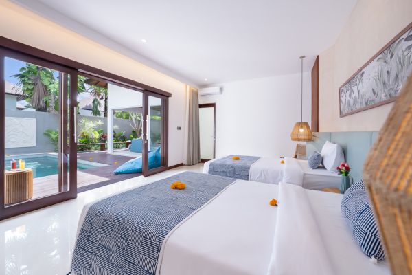 Serene Bali villa bedroom with twin beds, open sliding doors to a private pool, and tropical decor.