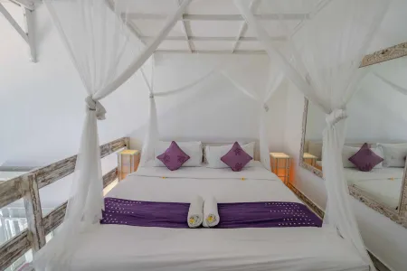 Cozy white canopy bed with purple pillows and throw in a Balinese-style loft bedroom.