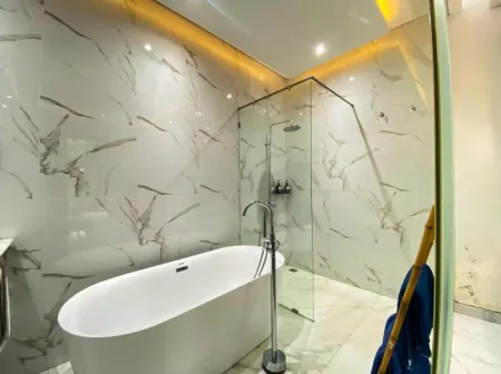Luxurious modern bathroom with white marble walls, freestanding oval bathtub, glass shower enclosure, and warm LED lighting. - Bali Villas