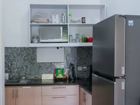 Modern corner kitchen with white cabinets, black granite countertop, stainless steel fridge, microwave, and assorted pantry items. - Bali Villas