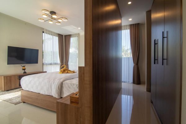 Modern bedroom interior with wooden bed, TV on wall, sheer curtains, and built-in wardrobe.