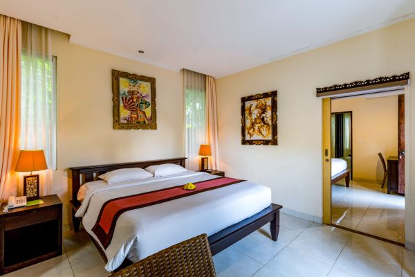 Spacious Balinese villa bedroom with king-sized bed, tropical artwork, sheer curtains, and garden views.