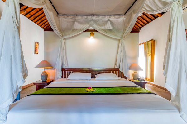 Luxurious Balinese bedroom with white canopy bed, wooden accents, and tropical decor.
