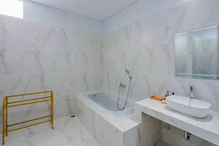 Modern white marble bathroom with freestanding bathtub, handheld shower, oval sink vanity, and mirror. - Bali Villas