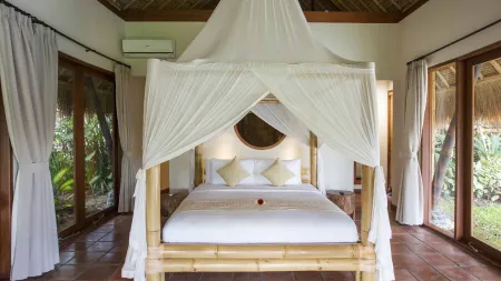 Elegant bamboo four-poster bed with white canopy in a tropical Balinese bedroom overlooking lush greenery.