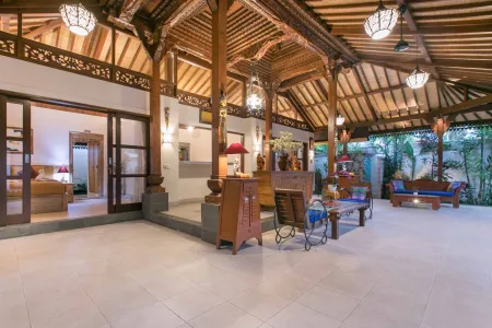 Spacious open-air Balinese pavilion with intricate carved wooden beams, hanging lanterns, rattan furniture, and tropical garden views. - Bali Villas