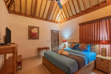 Cozy Balinese bedroom with thatched roof, wooden king bed, TV, and tropical artwork.