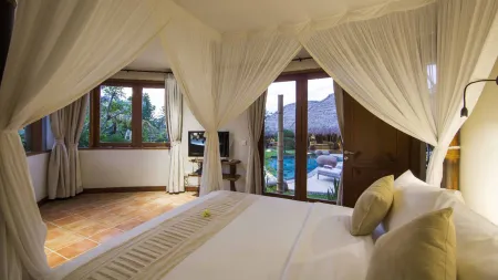 Luxurious tropical bedroom with white canopy bed, open doors to infinity pool, and lush garden views.
