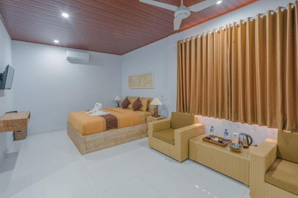 Cozy tropical hotel bedroom with wooden king bed, orange bedding, ceiling fan, rattan chairs, and large window curtains.