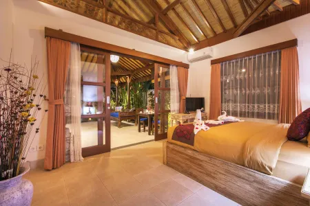 Spacious Balinese-style bedroom with wooden king bed, sliding doors to tropical patio, and elegant neutral decor.