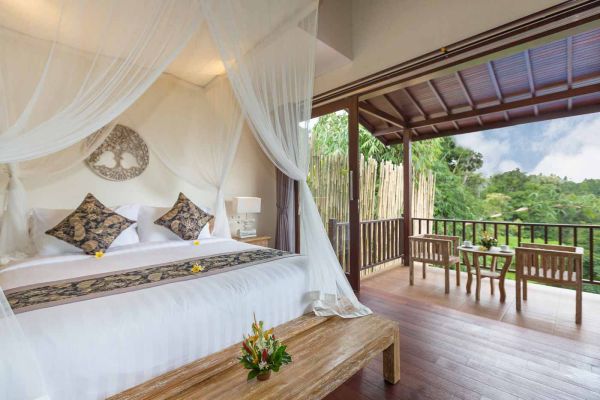 Luxurious Balinese canopy bed in a tropical villa bedroom with open balcony view of lush jungle greenery.