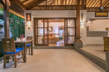 Spacious Balinese villa interior with open wooden dining area, sliding doors to cozy bedroom, and tropical plants.