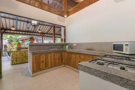 Spacious Balinese kitchen with wooden cabinets, granite counters, gas stove, and open tropical veranda view - Bali Villas