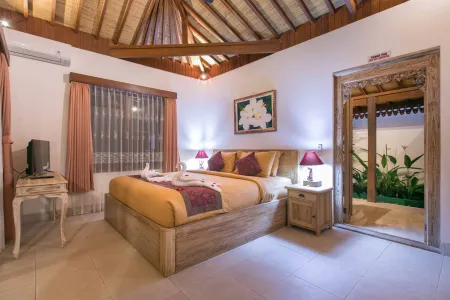 Cozy Balinese villa bedroom with wooden four-poster bed, floral accents, thatched ceiling, and open door to lush garden.