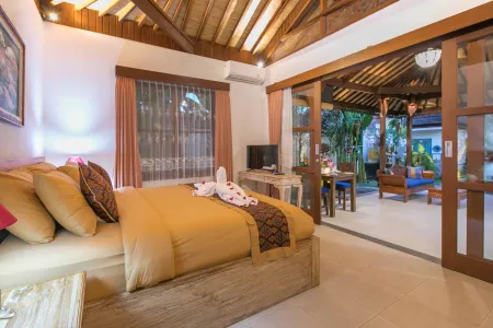 Luxurious Balinese villa bedroom with wooden beamed ceiling, king bed in warm tones, and sliding doors to lush garden view.