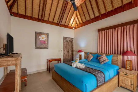 Luxurious Balinese bedroom with thatched wooden ceiling, elevated blue bed adorned with swan towel, pink curtains, and tropical decor.