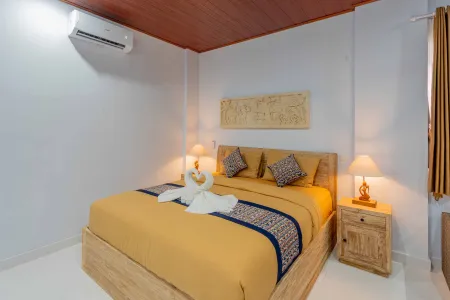 Cozy Balinese bedroom with king-sized wooden bed, yellow bedding, swan-shaped towel, bedside lamps, and tropical decor.
