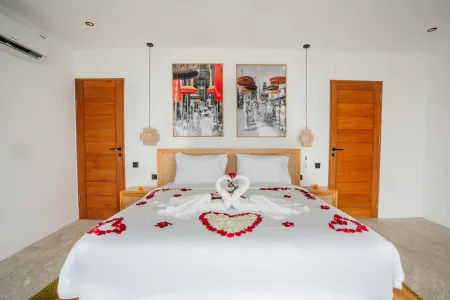 Romantic Bali villa bedroom with heart-shaped swan towel art and red rose petals scattered on a white king bed.