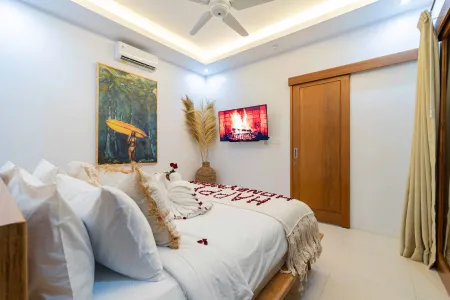 Romantic tropical bedroom with rose petal-strewn white bed, surfer wall art, pampas grass decor, and wooden accents.