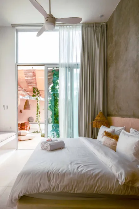 Bright, airy bedroom with white duvet bed, sheer curtains, and open doors to tropical pool patio.