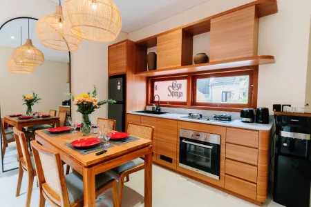 Modern Balinese-style kitchen and dining area with wooden cabinets, rattan pendant lights, set table, and "Ola Ola Soup" signage. - Bali Villas