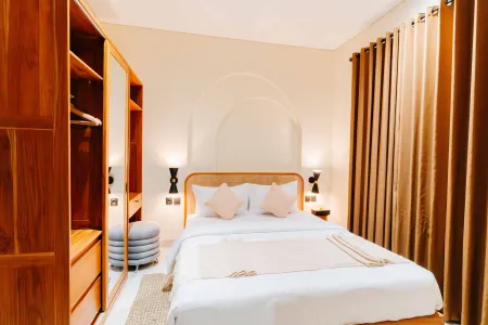 Cozy wooden bedroom interior with a neatly made queen bed, pink pillows, mirrored wardrobe, wall sconces, and beige curtains.
