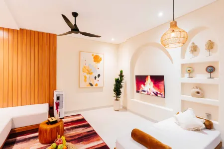 Modern tropical bedroom interior with wooden accents, cozy bed, potted plant, fireplace TV, and woven lighting.