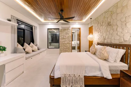 Spacious tropical villa bedroom with wooden king bed, white linens, ceiling fan, and large dark-tinted windows at night.