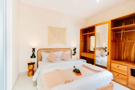 Cozy Balinese-style bedroom with wooden bed, pink bedding, woven wall art, and mirrored wardrobe.