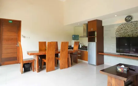 Spacious modern kitchen and dining area in a tropical villa, featuring wooden table, chairs, cabinets, and wall-mounted TV. - Bali Villas