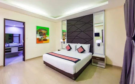 Spacious luxury hotel bedroom with king bed, mirrored headboard, vibrant wall art, and open en-suite bathroom. - Bali Villas