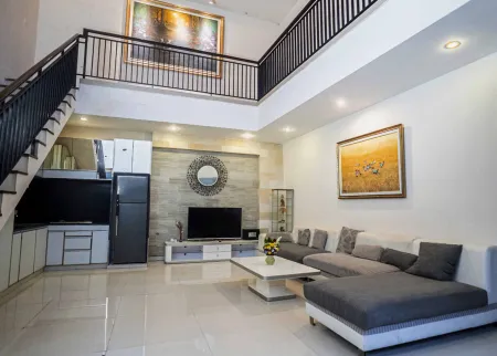 Spacious modern living room with open kitchen, gray sectional sofa, flat-screen TV, and wrought-iron staircase to mezzanine. - Bali Villas