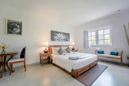 Serene Balinese-style hotel bedroom with wooden bed, white linens, abstract wall art, bamboo accents, and large windows overlooking tropical greenery. - Bali Villas