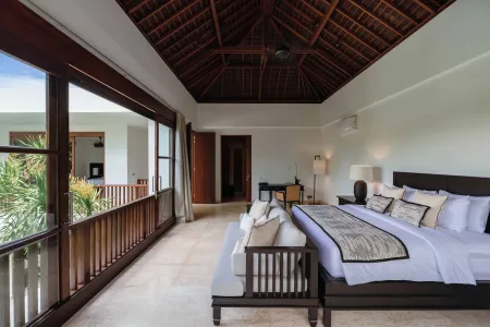 Spacious Balinese villa bedroom with king bed, thatched ceiling, open balcony to tropical views, and wooden accents.