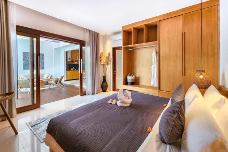 Spacious Balinese bedroom with king bed topped by a towel swan, wooden wardrobe, and open sliding doors to outdoor lounge.