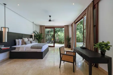 Spacious tropical bedroom with king bed, sliding glass doors to lush garden, wooden furniture, and potted plants.