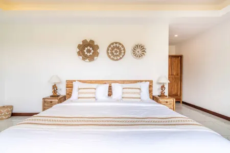 Serene Balinese bedroom with white king bed, woven rattan wall decor, wooden nightstands, and tropical accents.