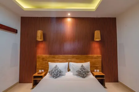 Cozy modern bedroom with wooden headboard, white bedding, gray pillows, wooden lamps, and slatted reddish-brown accent wall under green LED ceiling lights.