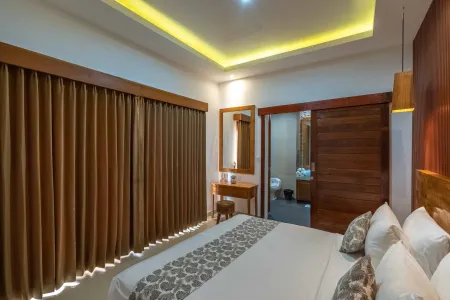 Spacious Balinese-style bedroom with wooden accents, king bed, sheer curtains, and open en-suite bathroom.