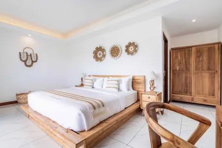 Spacious Balinese bedroom with wooden platform bed, woven sun decor, and natural teak furniture.