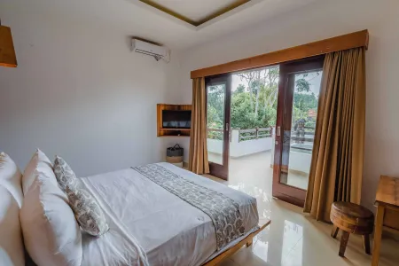 Serene Balinese bedroom with white king bed, wooden accents, and sliding doors to lush tropical balcony.