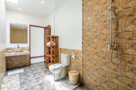 Modern tropical bathroom featuring brick-tiled shower, wooden vanity sink, toilet, and woven accents. - Bali Villas