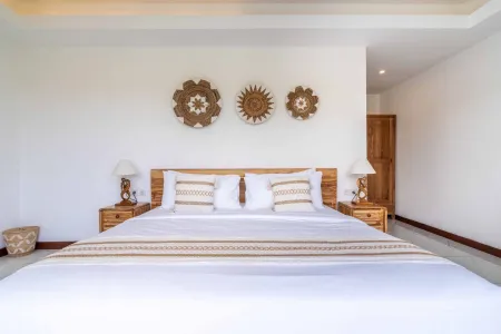 Cozy Balinese bedroom with white linens on wooden bed, rattan wall art, and bedside lamps.