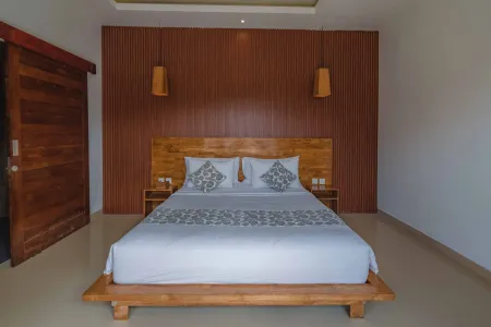 Cozy tropical bedroom with low wooden platform bed, white patterned linens, pillows, nightstand lamps, and warm wood-paneled walls.