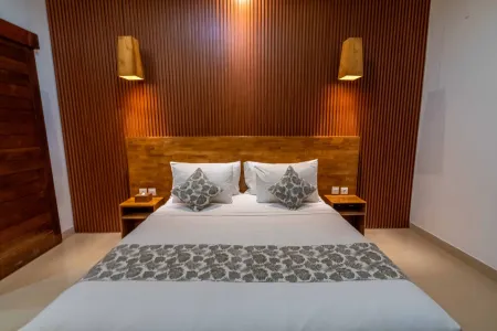 Cozy Balinese-style bedroom with wooden slat walls, king bed in white linens, gray patterned pillows, and wall-mounted lamps.