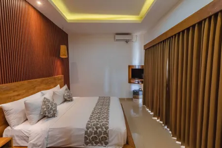 Spacious tropical bedroom with wooden slat walls, king bed in white linens, air conditioner, and beige curtains. - Bali Villas
