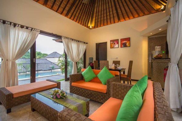 Spacious Balinese villa living room with orange wicker sofas, green cushions, wooden accents, and poolside balcony views. - Bali Villas