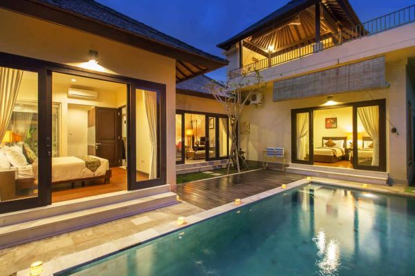 Luxurious Balinese villa at dusk with private pool, open bedrooms, and warm ambient lighting.