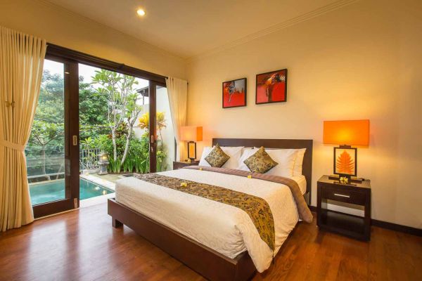 Luxurious tropical bedroom with wooden bed, sheer curtains, and sliding doors opening to a private pool and lush garden.